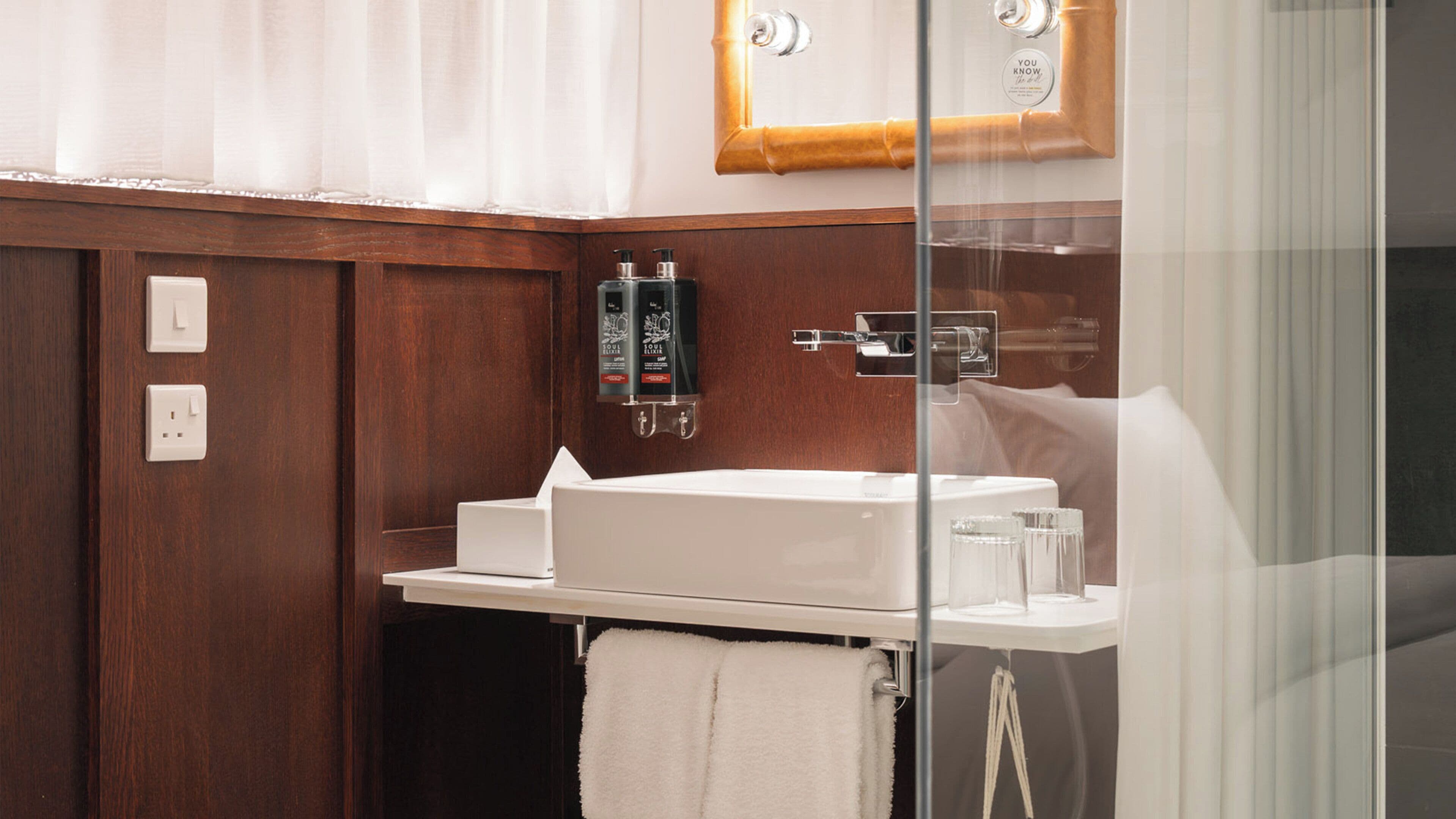 A bathroom with a white sink, a towel, a glass shower enclosure, and a wooden panel wall.