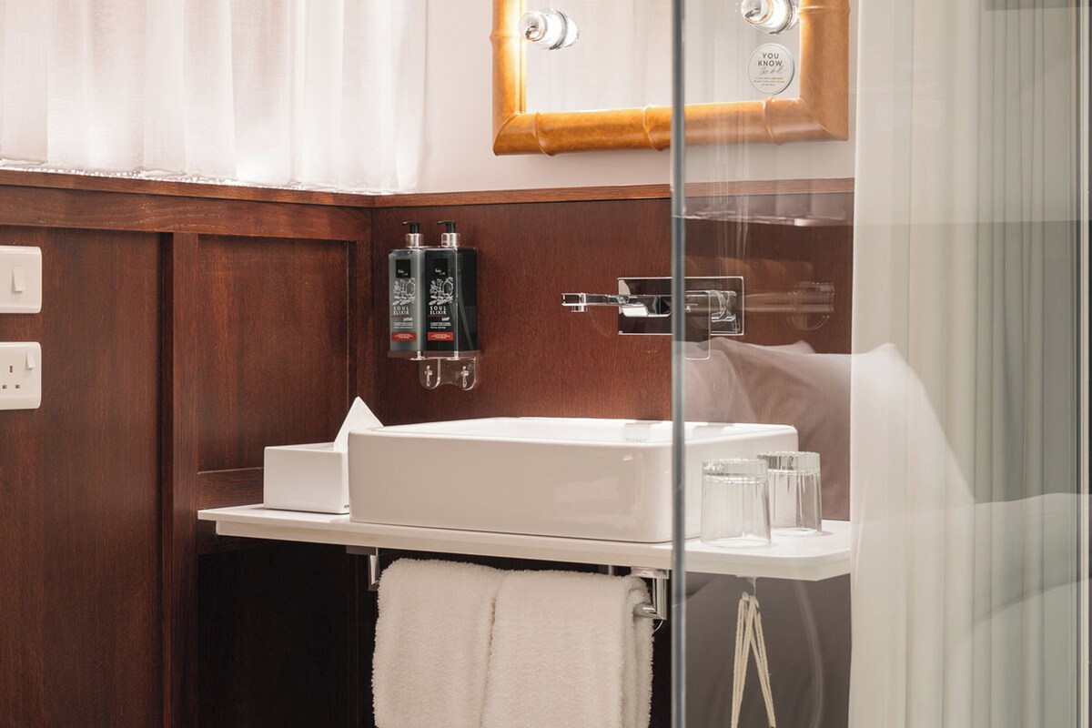 A bathroom with a white sink, a towel, a glass shower enclosure, and a wooden panel wall.