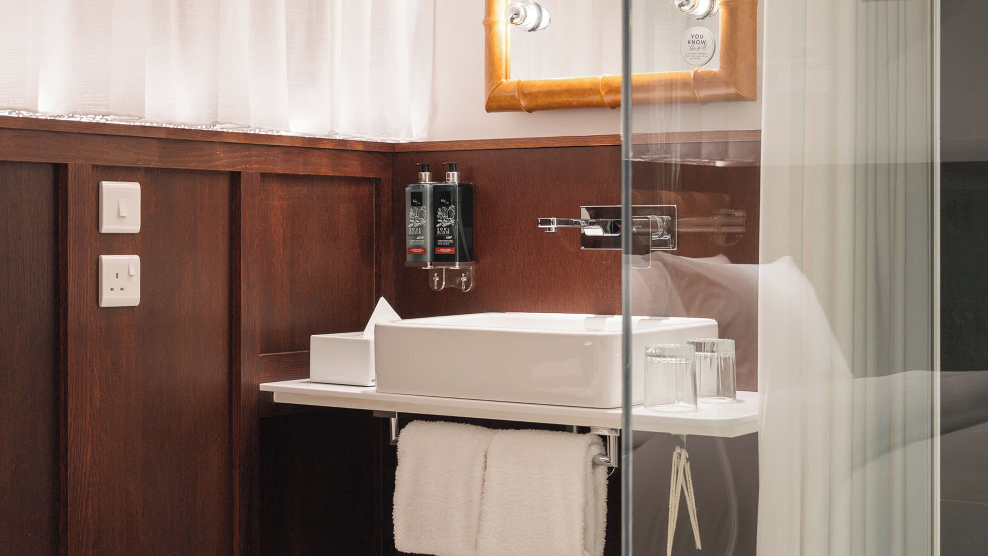 A bathroom with a white sink, wooden paneling, a glass shower enclosure, and a towel rack.