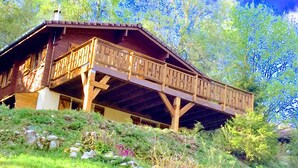 A chalet with a wooden balcony, surrounded by greenery and a sign indicating 'Chemin des Sorbiers'.
