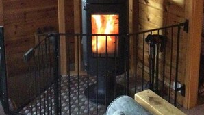 A cozy room with a wood-burning stove, a television mounted on the wall, and a wooden bench.