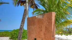Un patio frente a la playa con una palmera, suelo de baldosas y una pared blanca con un ventanal pequeño.