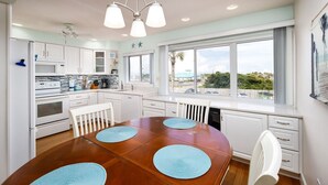 Una cocina moderna con armarios blancos, una isla grande y una zona de comedor con mesa de madera y posavasos azules.
