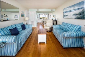 A living room with striped sofas, a wooden coffee table, and a view into the kitchen. - Seaspray Condos - 108D (Fort Walton Beach)