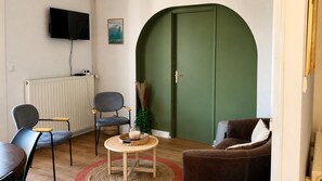 A living room with a green door, a television mounted on the wall, and a chair with a basket on the floor.