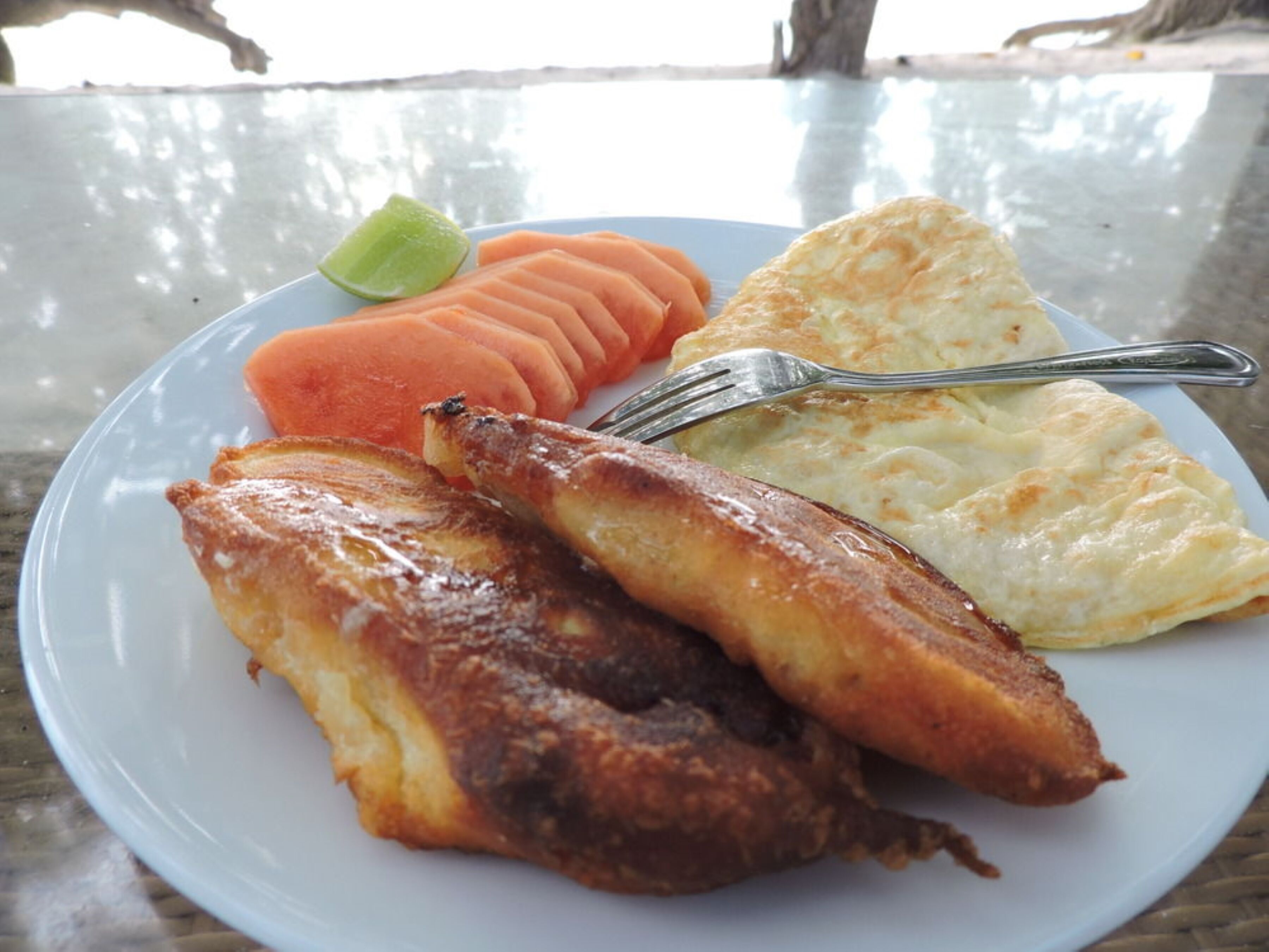 A plate with fried fish, a slice of toast, and a carrot on a glass table.