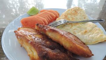 A plate with fried fish, a slice of toast, and a carrot on a glass table.