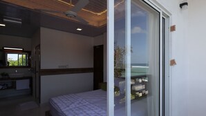 A modern bedroom with a large bed, a bathroom with a sink and mirror, and a view of the ocean through a sliding door.