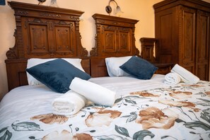 Een net opgemaakt bed met bloemenbeddengoed, twee donkerblauwe kussens en een houten hoofdbord.
