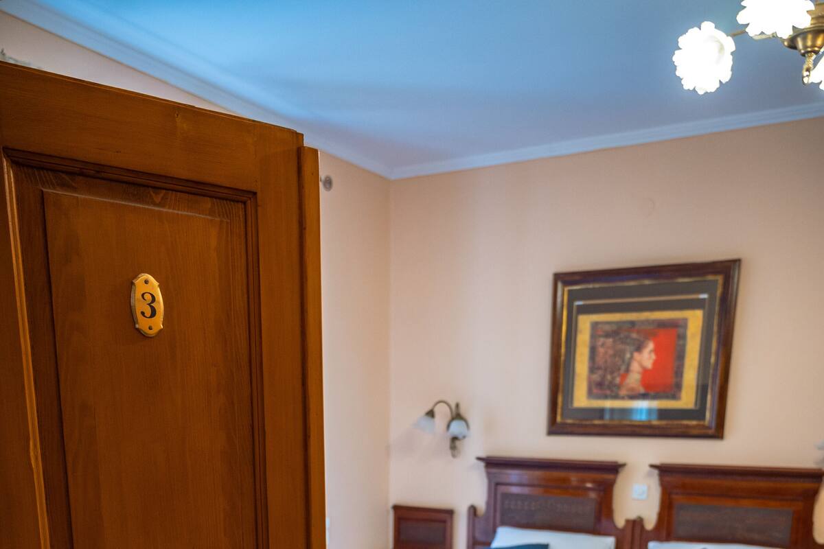A room with two wooden beds, a wooden door, a herringbone floor, and a framed picture on the wall.