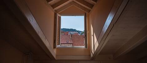 Un tragaluz en una habitación con vigas de madera y vistas a edificios con tejados rojos.