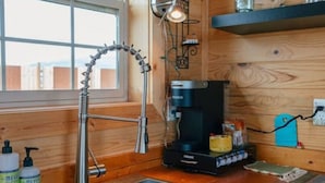 A wooden cabin interior with a sink, a coffee maker, and a shelf with glasses.