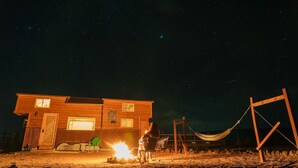 A wooden cabin with a fire pit, a hammock, and a starry night sky.