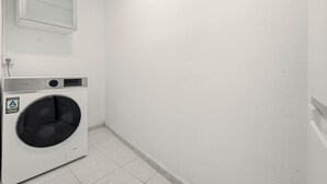 A laundry room with a front-loading washing machine, a wall-mounted mirror, and a tiled floor. - Chueca Central Residence (Madrid)