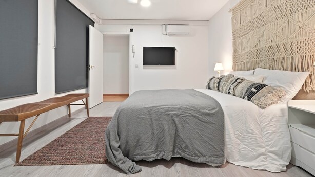 A modern bedroom with a bed, bedside table, bench, and a wall-mounted TV. - Chueca Central Residence (Madrid)