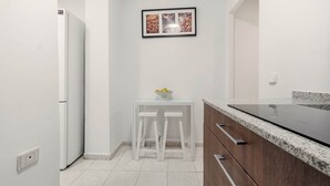 A modern kitchen with white cabinets, a granite countertop, and a small white table with stools. - Chueca Central Residence (Madrid)