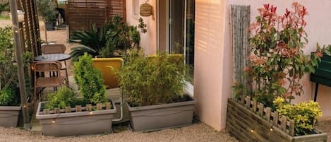 A building with a covered patio, outdoor seating, potted plants, and a sign indicating a restaurant.