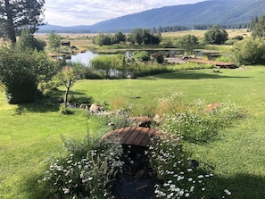 A rustic wooden structure in a lush green field with a pond and mountains in the background.