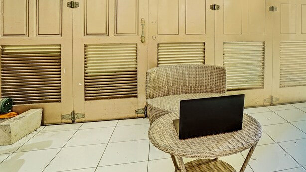 Una silla de mimbre con un ordenador portátil sobre una mesa redonda, una puerta cerrada con un pestillo y un suelo de baldosas.
