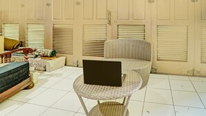 Una habitación con una silla de mimbre, un sofá y un ordenador portátil sobre una mesita.