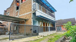 Un edificio de dos pisos con balcón, entrada protegida por reja y fachada de ladrillo.