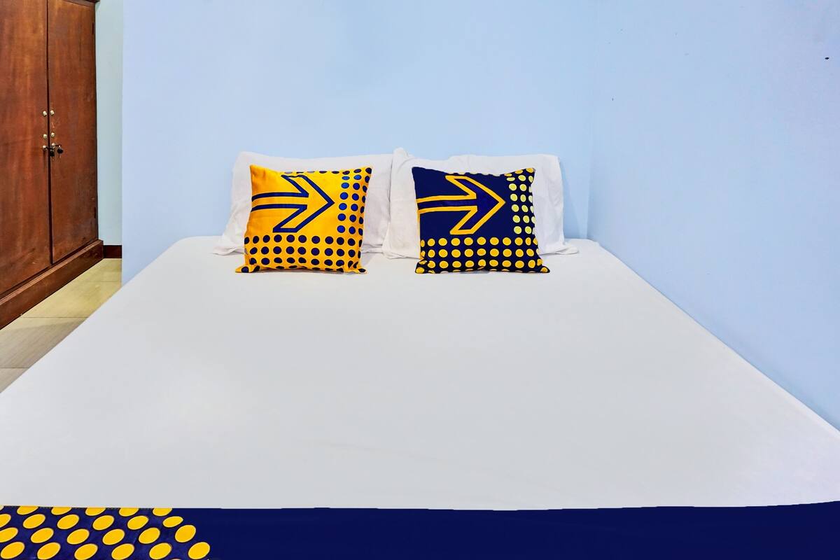 Una cama con ropa blanca y dos almohadas con motivos azules y amarillos.