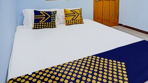 Una cama con colchón blanco, colcha de lunares azules y amarillos, y dos almohadas con diseños similares.