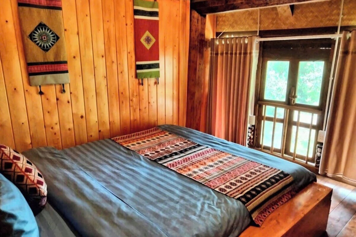 Una habitación de madera con una cama, un banco y una ventana con cortinas.