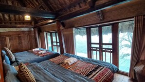 Una habitación rústica de madera con dos camas, ventanas amplias y techo de madera.