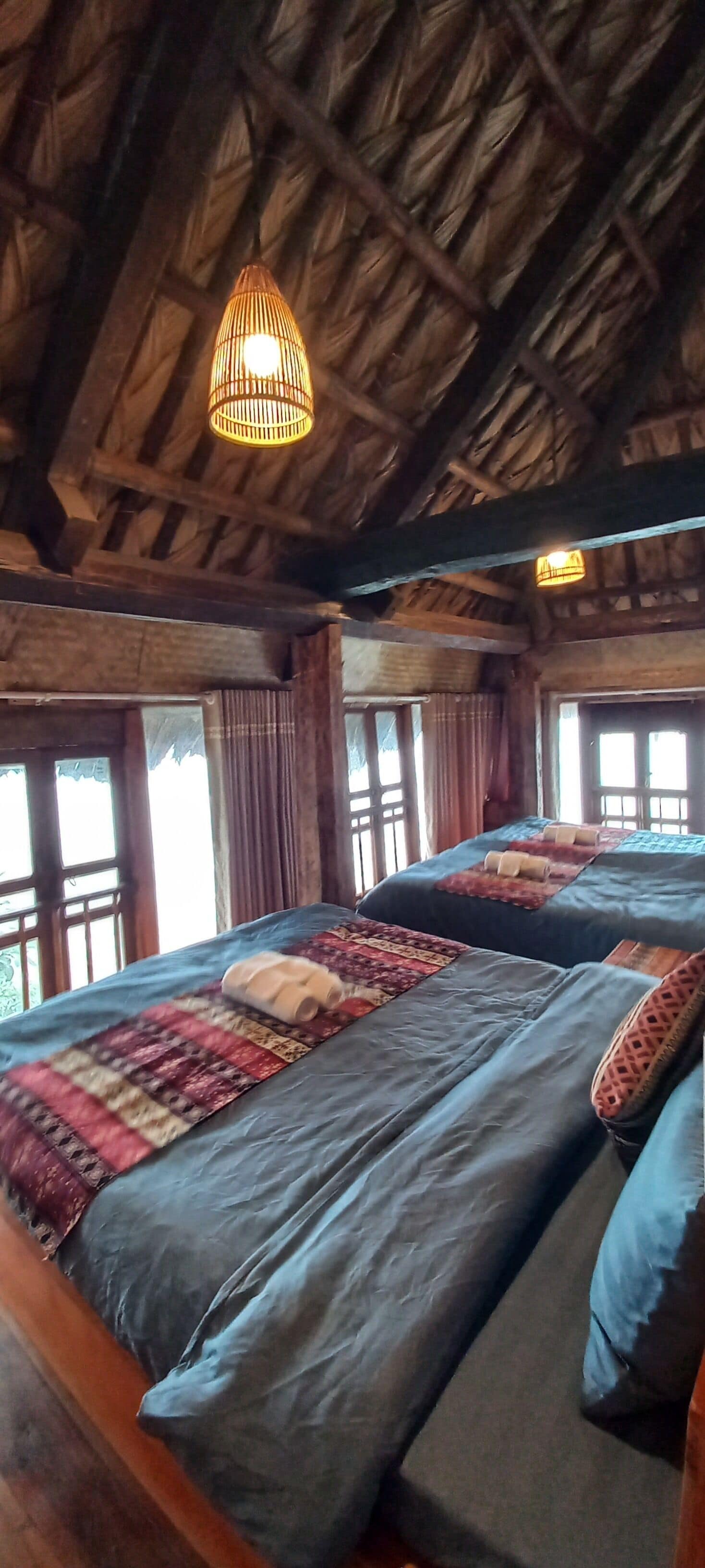 A room with two beds, wooden beams on the ceiling, and a hanging light fixture.
