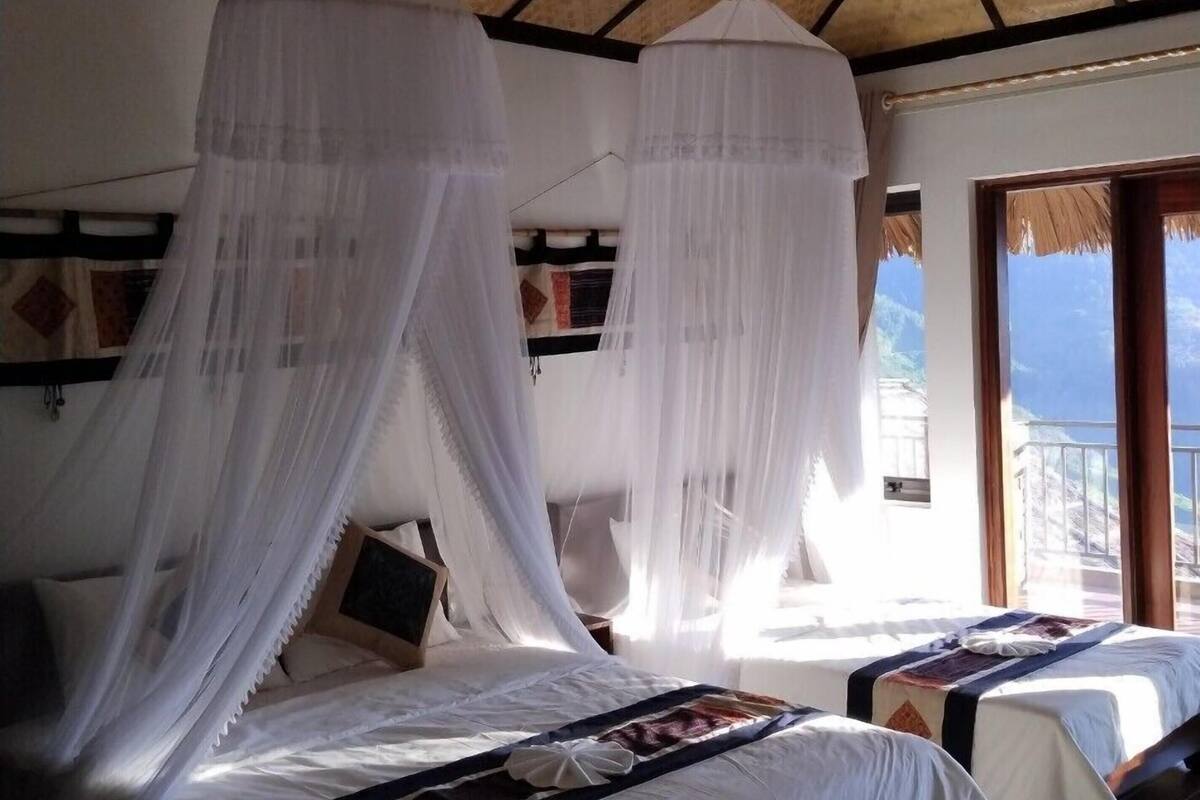 Quarto com duas camas, cada uma com dossel, uma janela grande e vista para o exterior.
