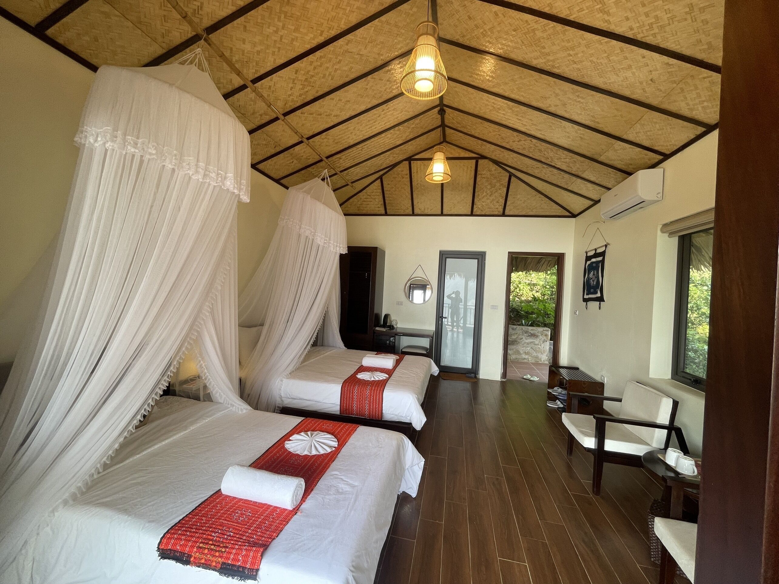 A room with two beds, each with white bedding and red decorative pillows, a wooden floor, and a ceiling with exposed beams.