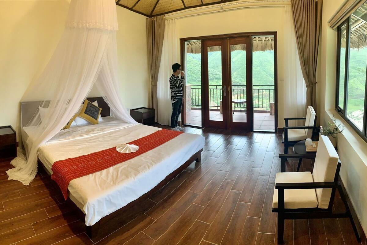 Quarto com cama de dossel, varanda com vista e área de jantar com uma cadeira.