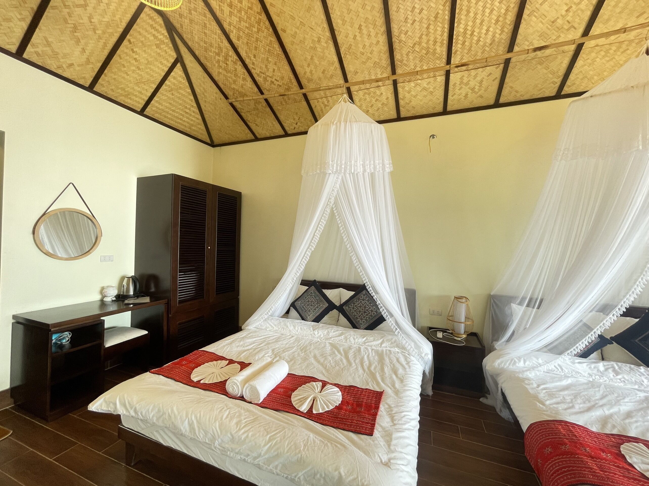 A room with two beds, each with a canopy, a wardrobe, a bedside table, and a mirror.