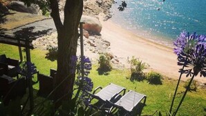 Une vue sur la plage avec un fauteuil de relaxation et une table, le tout entouré de verdure et d’un arbre.