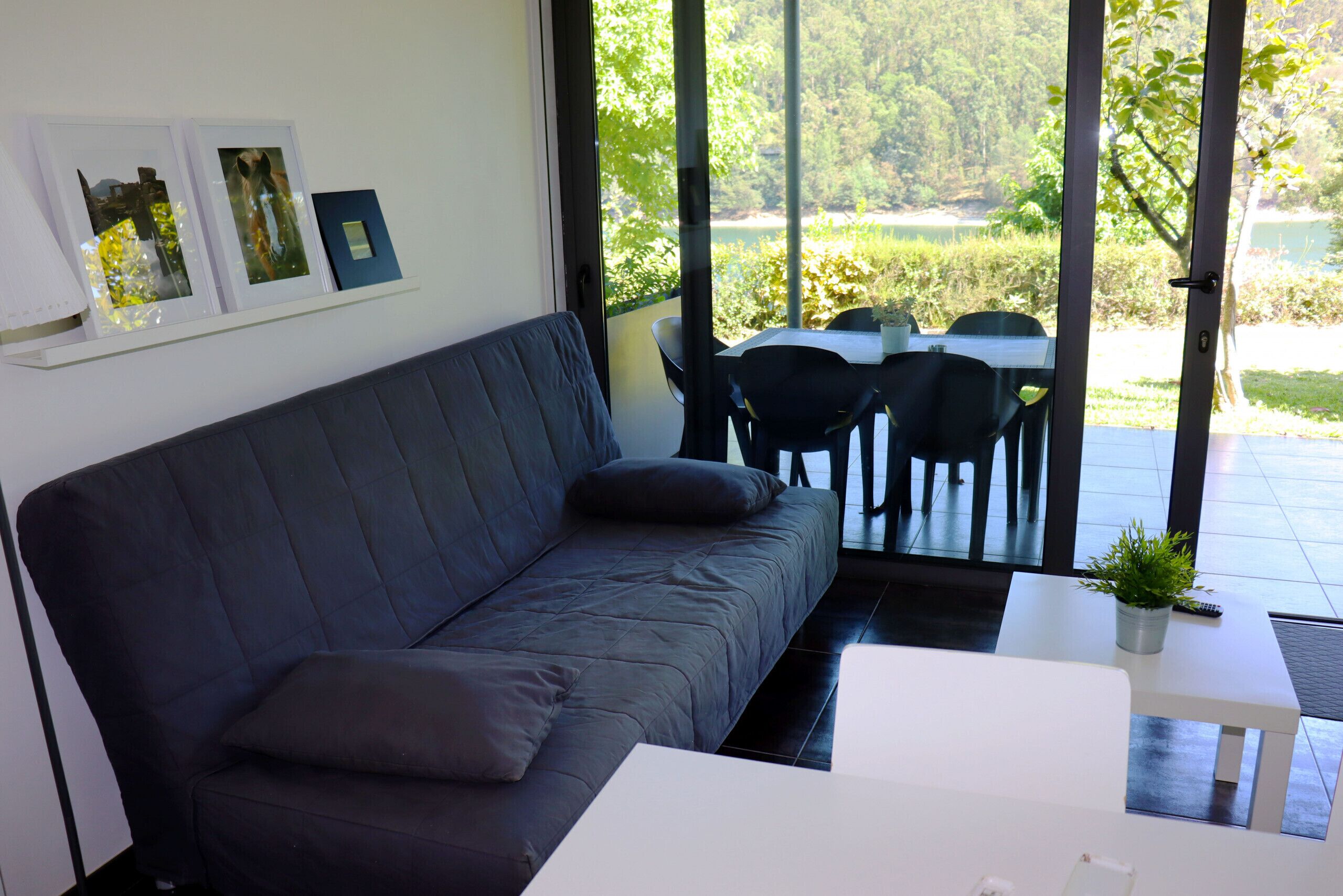 A modern living room with a dark-colored sofa, a white coffee table, and a view of a garden through large windows.