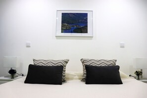 A neatly arranged hotel room with a bed, two pillows, a nightstand, a lamp, and a framed picture on the wall.