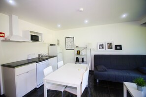 A compact living space with a kitchenette, a dining table, a sofa, and a small bookshelf.