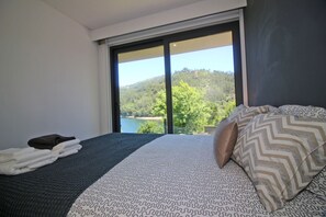 A bedroom with a large window, a bed with patterned bedding, and a view of a lake and hills. - Apartment with Private Beach in Gerês (Gerês)