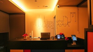 Bancada de recepção de hotel com design moderno, apresentando uma tela digital, um telefone e uma pequena planta.