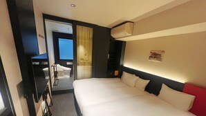 Quarto de hotel com uma cama grande, banheiro com vaso sanitário e chuveiro, e vista para o exterior.