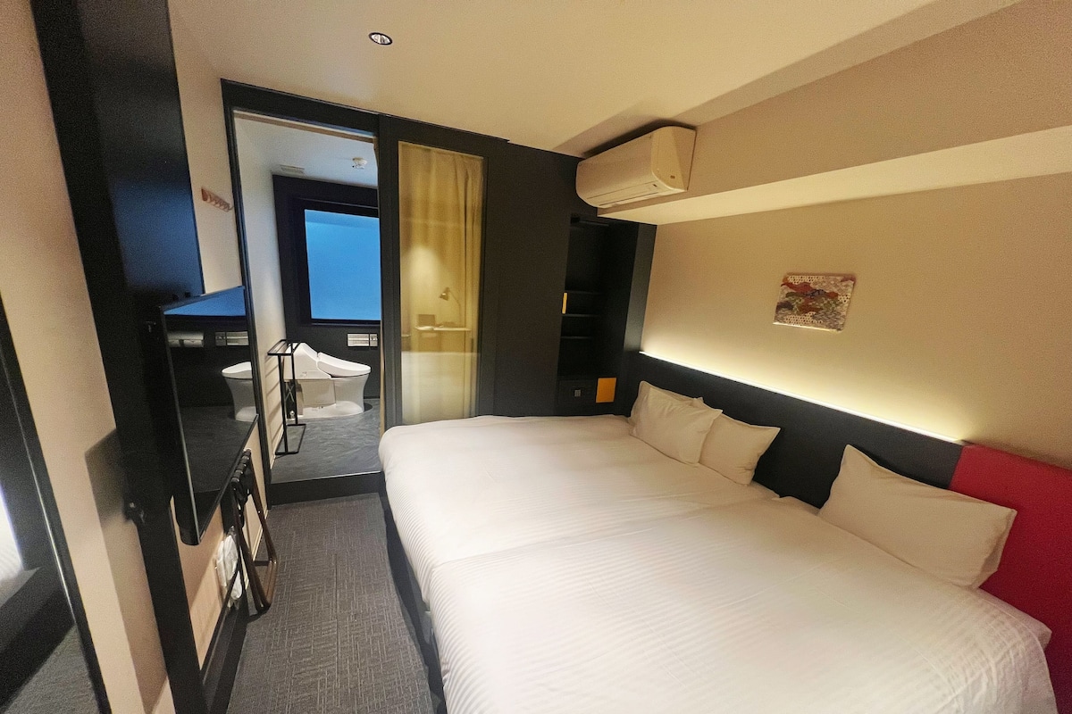 A hotel room with a large bed, a bathroom with a toilet and a shower, and a view of the outside.