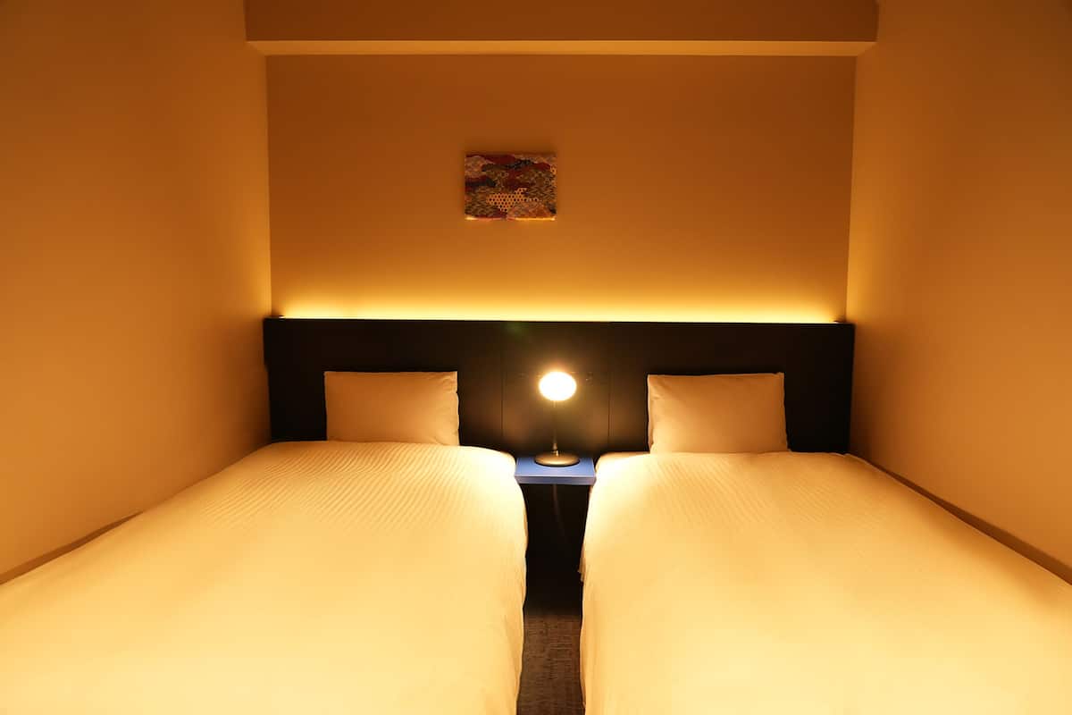 A twin room with two beds, a nightstand, and a wall-mounted lamp.