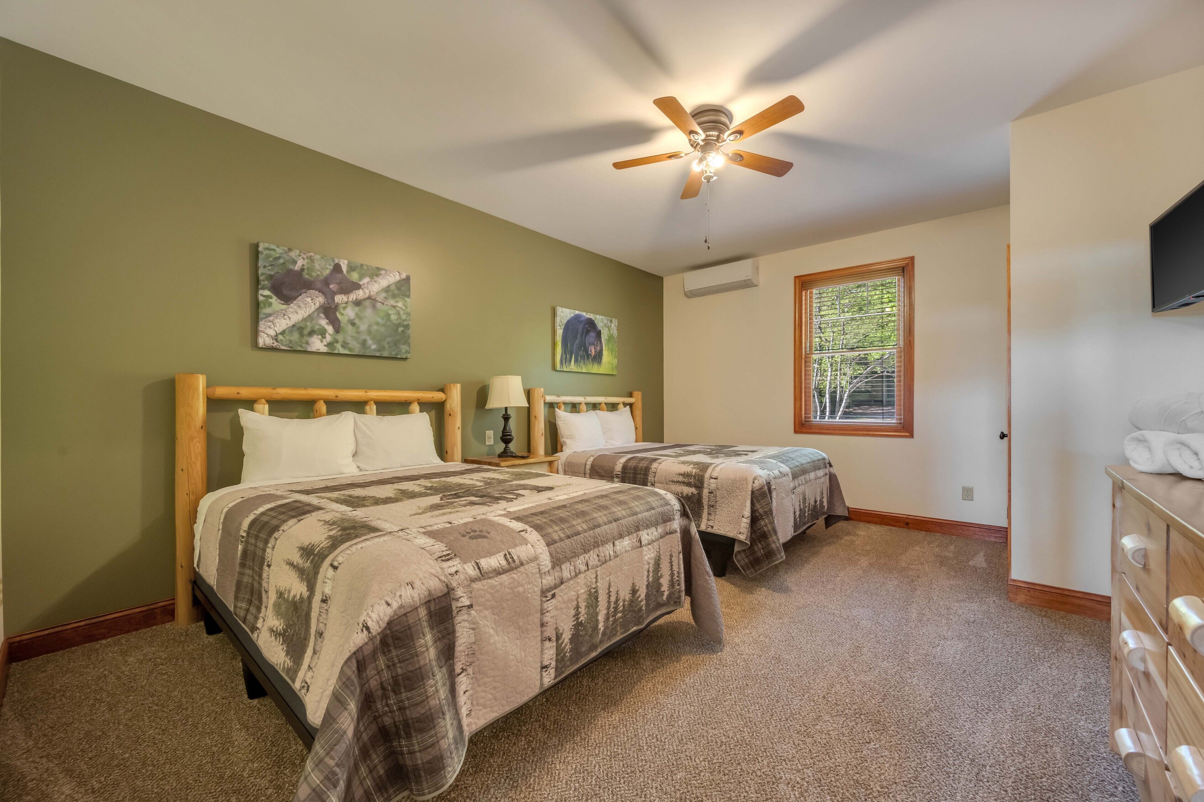A bedroom with two beds, a ceiling fan, a window, and artwork on the walls.