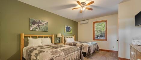 A bedroom with two beds, a ceiling fan, a window, and artwork on the walls.