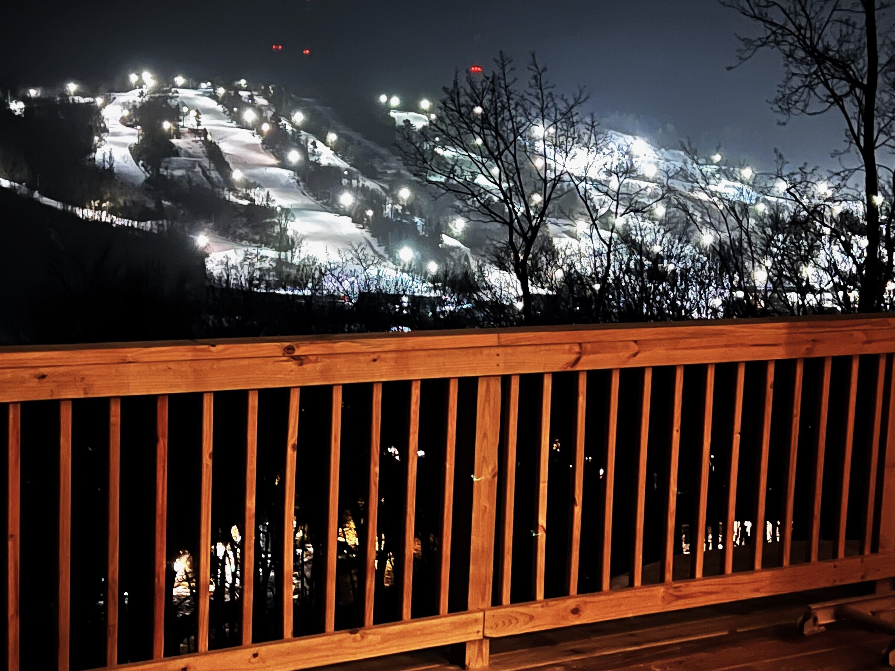 Eine Holzterrasse mit Geländern, die einen mit Schnee bedeckten Hang mit Lichtern überblickt.