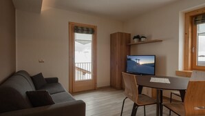Ett modernt vardagsrum med en soffa, ett matbord med stolar, en tv och ett träskåp.