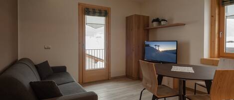 A modern living room with a sofa, a dining table with chairs, a television, and a wooden cabinet.