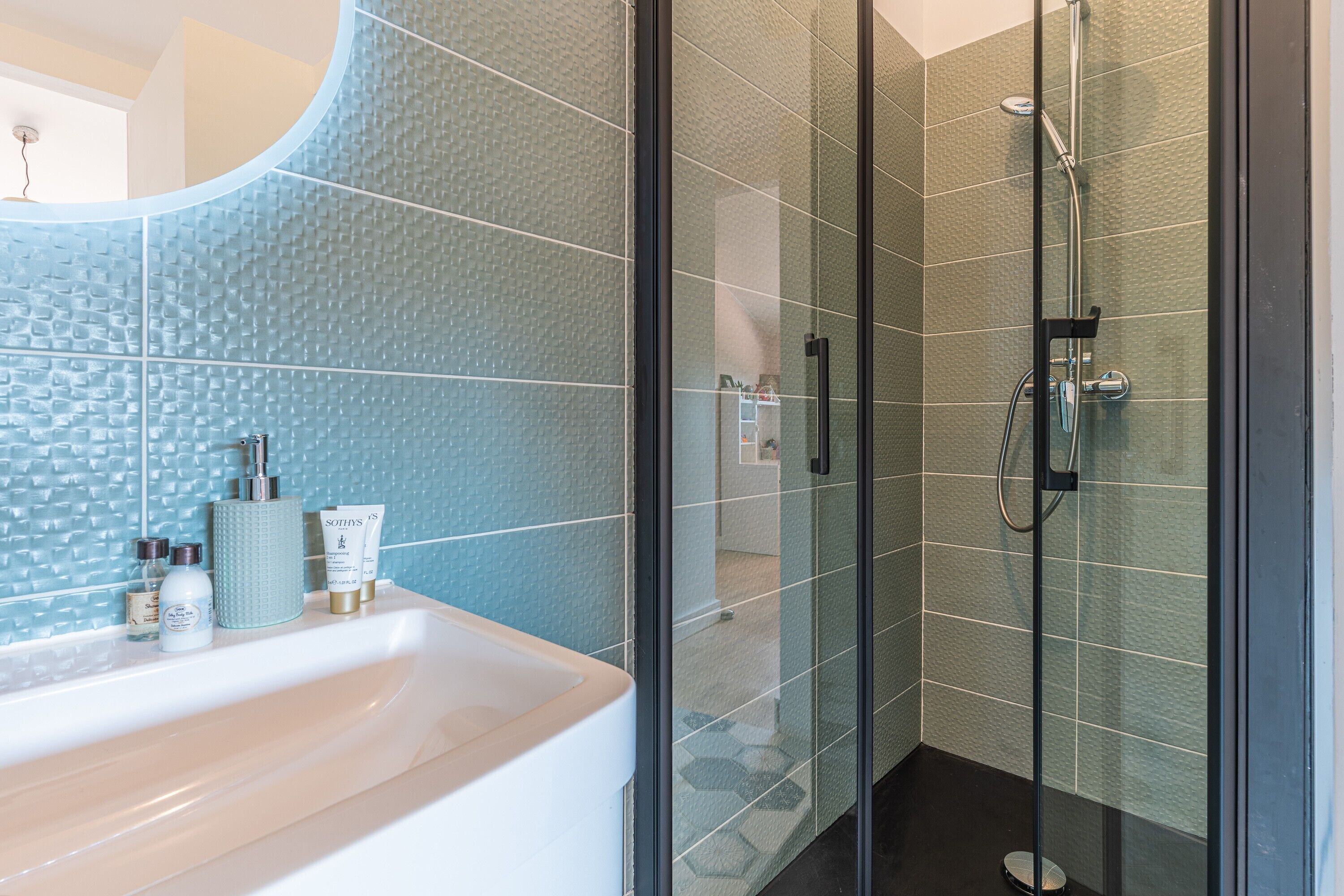 Un baño con cabina de ducha de vidrio, un lavamanos blanco con artículos de aseo y una pared con textura.