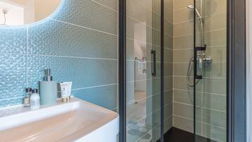 Un baño con cabina de ducha de vidrio, un lavamanos blanco con artículos de aseo y una pared con textura.